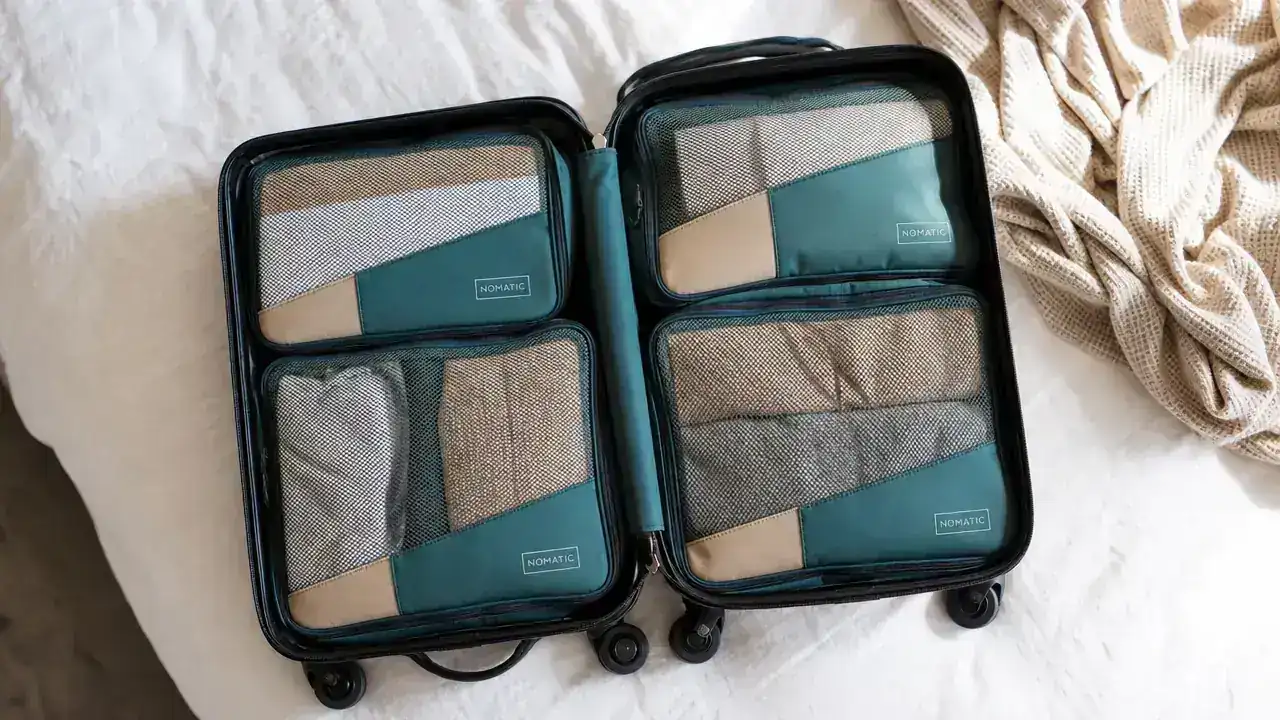 Open carry-on suitcase on a bed filled with neatly organized packing cubes, a folded week of clothes visible through mesh tops