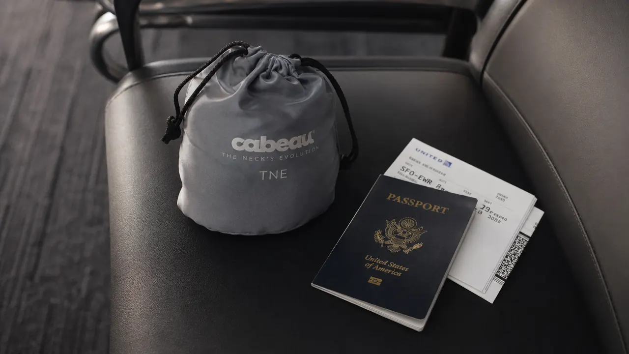 Travel neck pillow packed into its drawstring carry bag next to a passport and boarding pass