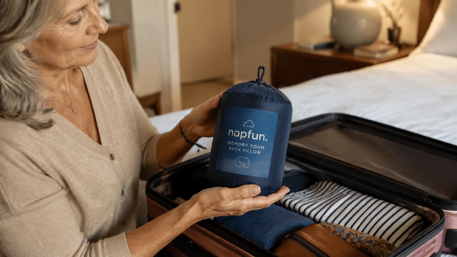 napfun memory foam neck pillow held in one hand over an open carry-on bag, ready to pack